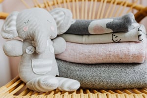 A stuffed grey baby elephant toy sits next to some folded towels