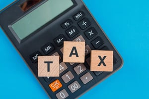 wooden cubes spelling out tax sit on top of a calculator on a blue background