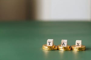 Three wooden cubes spelling out tax sit on gold coins atop a green table