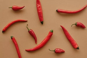 An assortment of vibrant red chili peppers scattered on a brown background, showcasing their varying shapes and sizes.