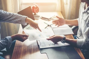 Two professionals discussing business reports and charts at a desk, emphasizing collaboration and strategy in a modern office setting.