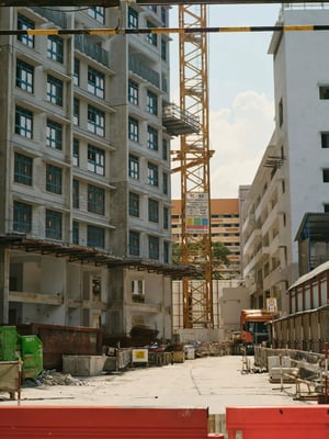 Construction site featuring tall buildings, a yellow crane, and construction materials under a clear blue sky.