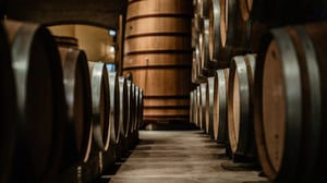 Two rows of whiskey barrels face each other in a low lit room