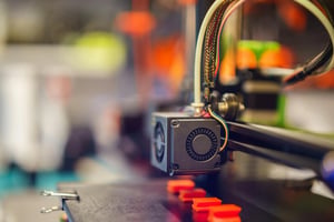 Close-up of a 3D printer's extruder and cooling fan, showcasing vibrant colors and intricate design elements in a workshop setting.