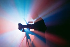 A silhouette of a photographer using a camera, surrounded by colourful light rays, creating a dramatic and artistic atmosphere.