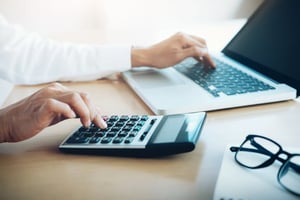 Man types at laptop and calculator on desk