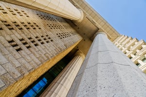 Architectural view of large stone columns and textured wall, showcasing modern design and structural elegance against a clear blue sky.