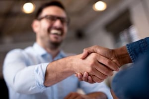 a smiling man in a blue shirt shakes another mans hand