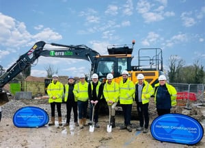 Group of construction workers in high vis stand in front of yellow digger on building site