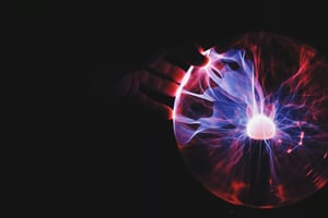 A hand reaching out to touch a glowing plasma ball, showcasing vibrant electric arcs and colourful energy patterns in a dark setting.