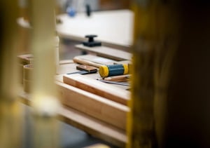 Close-up of woodworking tools on a workbench, showcasing a yellow and blue clamp, wooden pieces, and measuring tools in a workshop.