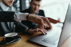 Two business professionals collaborating over a laptop, discussing ideas with a cup of coffee on the table, in a modern workspace.