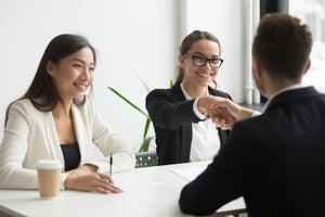 Three professionals meeting across a table, with one person shaking hands after what appears to be a successful interview or business meeting.